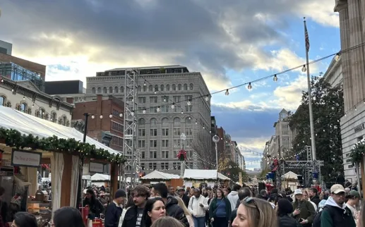 Holiday market scene in Downtown DC with crowds, festive decorations, and string lights.
